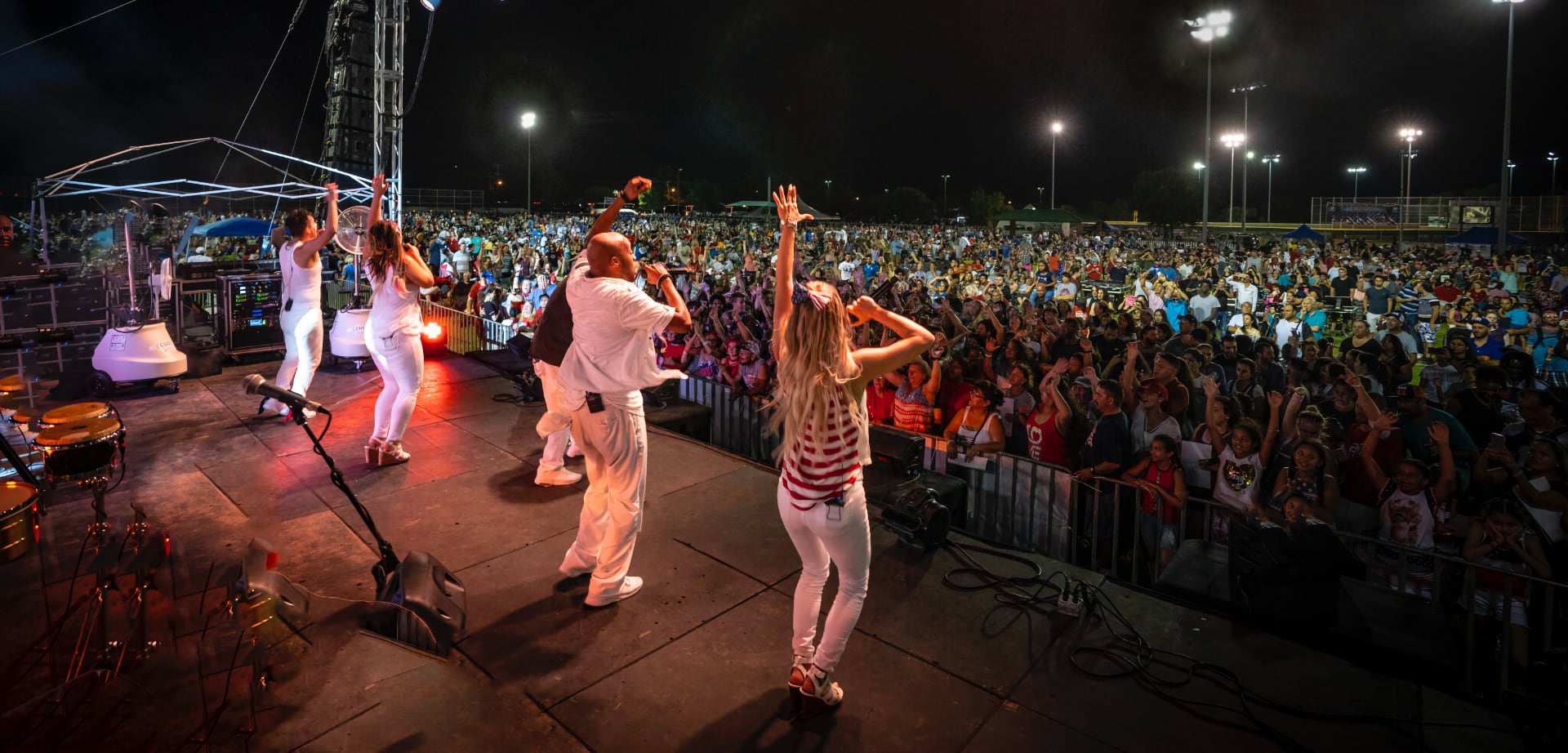 Band performing on stage at night before a cheering crowd at an outdoor concert.
