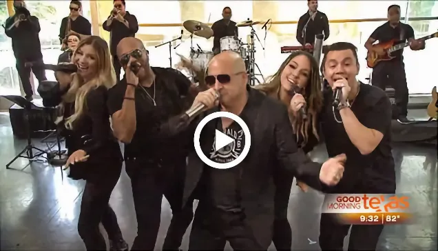Band members singing energetically on stage with instruments in the background.