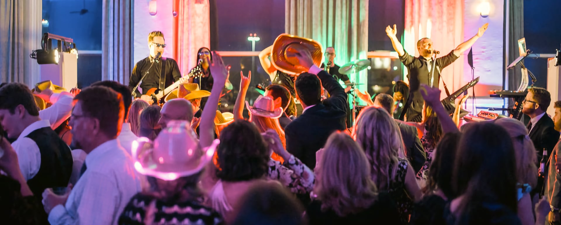 Crowd dancing at a lively indoor concert with colorful lights and a band performing on stage.