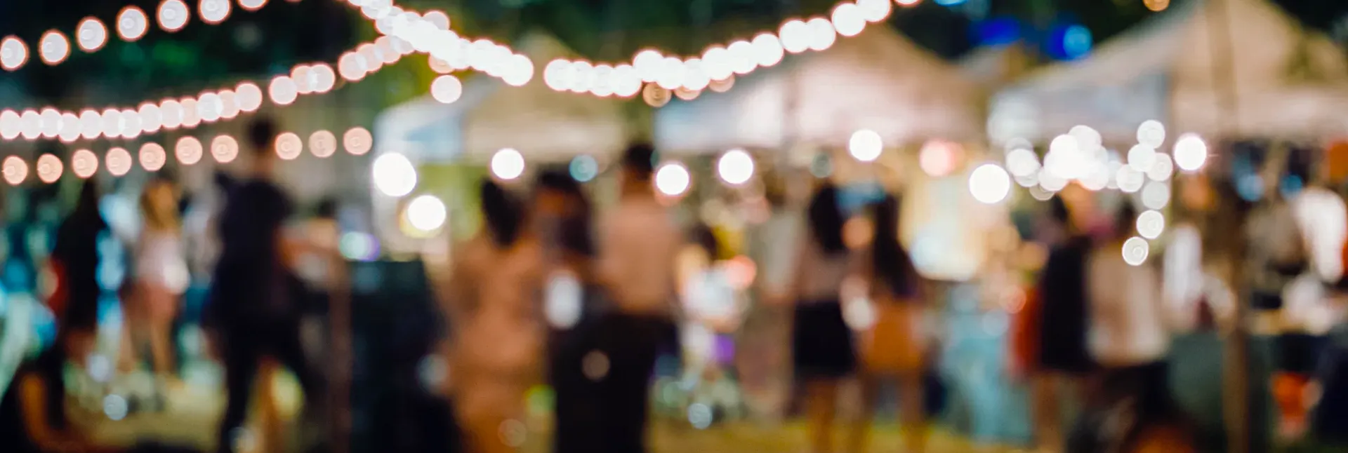Blurry outdoor festival scene with people and string lights at night.