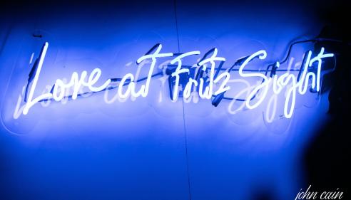 Blue neon sign reads "Love at First Sight" against a dark background.