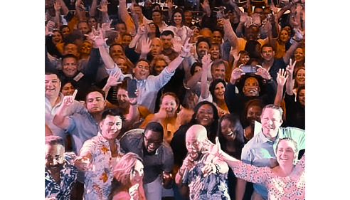Large group of people smiling and waving at a lively indoor event.
