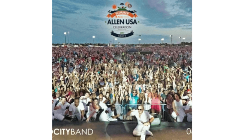 Large outdoor crowd at a festival, with musicians in white uniforms posing in front.