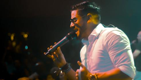 Man in a white shirt singing passionately into a microphone on stage.