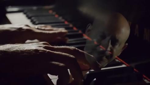 Hands playing piano keys with a man’s face reflected on the glossy surface.