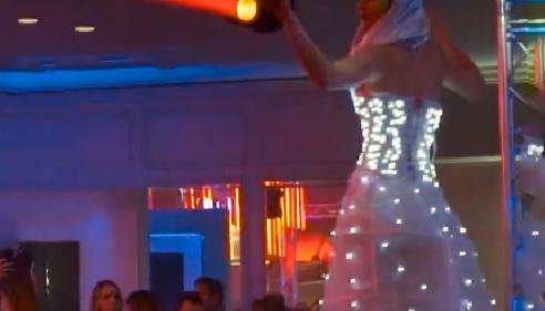 Performer in a glowing LED dress shines a spotlight over a crowd at an indoor event.