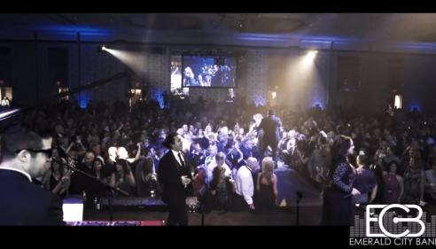Large crowd at a formal event with a band performing on stage under blue and yellow lights.