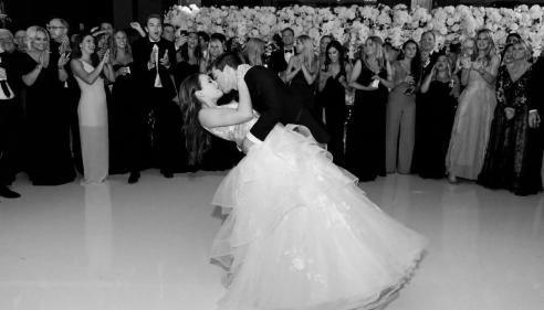 Bride and groom share a kiss on the dance floor surrounded by applauding guests.