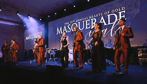 Band performing on stage under purple lighting at a masquerade gala event.