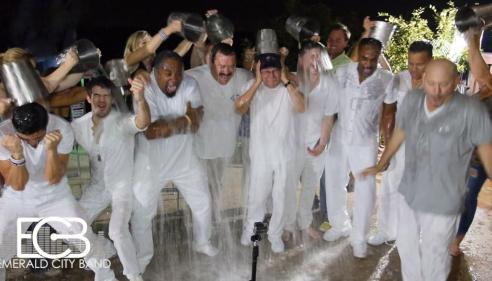 Group of people in white clothing doing the ice bucket challenge at night.
