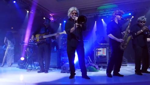Band performing on stage with colorful lighting and fog effects.