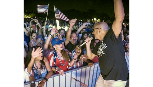 Singer performing on stage at night, hyped crowd reaching toward him.