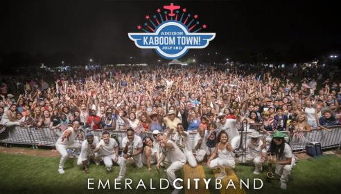 Emerald City Band posing in front of a large, cheering outdoor crowd at night.
