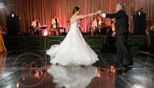 Bride and father dancing on a reflective floor with a live band in the background.