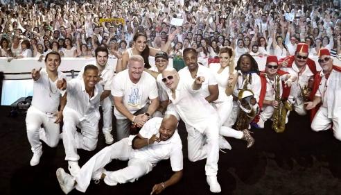 Members of Emerald City Band standing in front of a large crowd all dressed in white