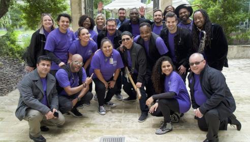 Group of people smiling outdoors, most wearing purple shirts, some in black jackets.