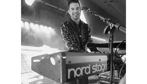 Smiling musician playing a Nord Stage keyboard on stage under bright lights.