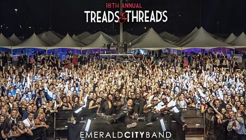 Large crowd at a nighttime outdoor event with tents and stage lighting.