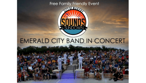 Outdoor concert with a band performing on stage and a large seated audience at sunset.