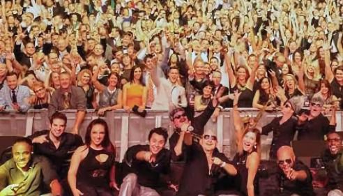 Members of Emerald City Band sitting on stage in front of a large crowd