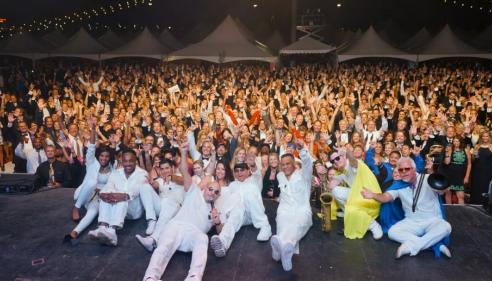 Performers in white pose on stage before a cheering crowd at a nighttime outdoor event.