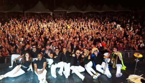 Members of Emerald City Band sitting on stage with a large crowd behind them