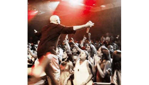 Performer on stage reaching out to an excited crowd under red stage lights.