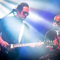 Two musicians performing on stage with dramatic lighting.