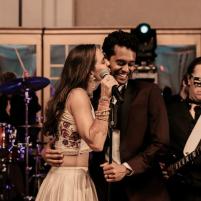 Woman and man singing into a microphone on stage with live band in background.