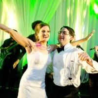 Bride and groom dancing joyfully at a wedding reception with live band and green lighting.