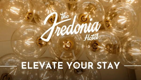 Cluster of hanging glass light bulbs with "Elevate Your Stay" and hotel logo overlay.