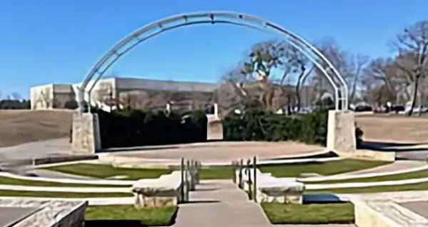Outdoor amphitheater with curved metal arch and tiered stone seating on a sunny day.