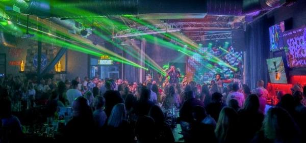 Crowded nightclub with colorful stage lights and people dancing and sitting at tables.