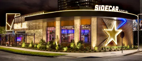 Modern restaurant with neon lights, large star decoration, and "SIDECAR" sign at night.