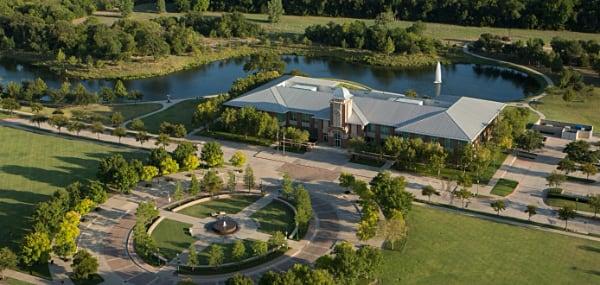 Aerial view of a building beside a pond surrounded by trees and a circular driveway.