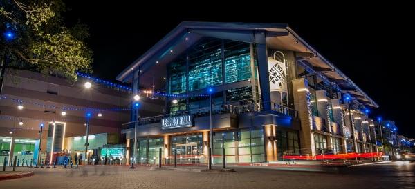 Modern building with glass front lit by blue lights at night, people near entrance.