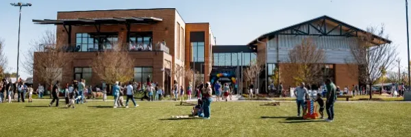People gathered on a grassy lawn in front of a modern brick building on a sunny day.