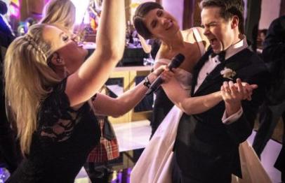 Bride and groom singing into a microphone at a lively wedding reception.