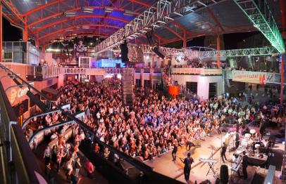 Large crowd gathered at an indoor concert with colorful stage lighting.