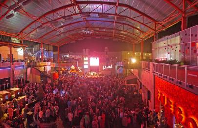 Large crowd gathered under a lit-up metal roof at a nighttime event or concert.