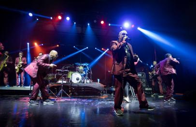 Band performing on stage with colorful lights and energetic musicians in suits.