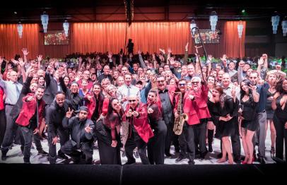 Large group of people smiling and posing together at an indoor event with warm lighting.