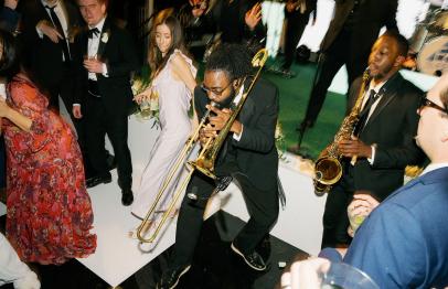 Musicians playing trombone and saxophone on a dance floor surrounded by people in formal attire.