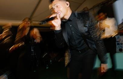 Singer in a black suit performing energetically on stage with a microphone.
