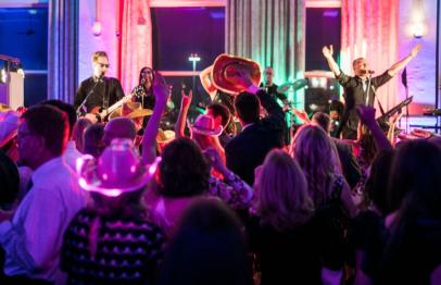 Crowd dancing at a lively indoor party with colorful lights and live band performing.