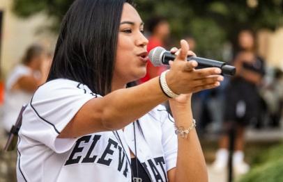 Woman singing passionately into a microphone outdoors, gesturing with her hand.