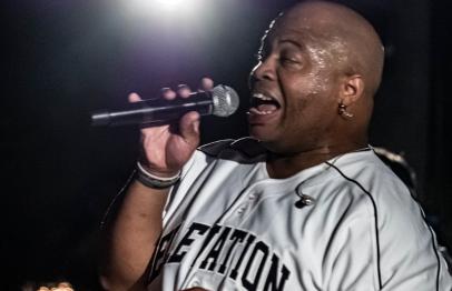 Man passionately singing into a microphone under stage lighting.