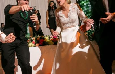 Bride and groom laughing while dancing at a lively wedding reception.