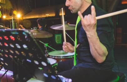 Drummer performing on stage, holding drumsticks and making a rock hand gesture.