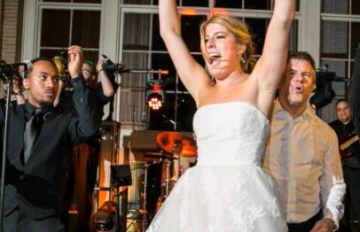 Bride in white dress dancing joyfully with guests at a wedding reception.